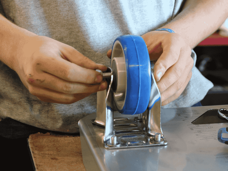 Montage d’une roulette en caoutchouc bleu sur roule-bac inox dans nos ateliers